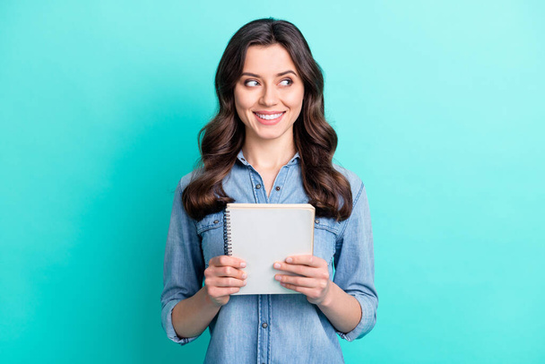 Photo of shiny pretty young lady dressed denim shirt smiling holding copybook looking empty space isolated teal color background - Φωτογραφία, εικόνα