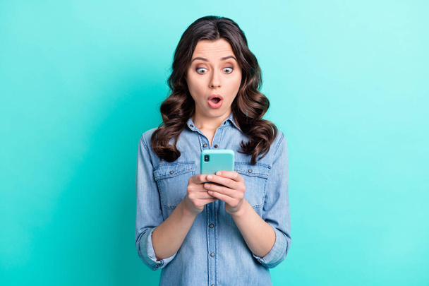 Foto de chica joven sorprendida mirada sorprendida leer navegar noticias falsas teléfono celular aislado sobre fondo de color turquesa - Foto, Imagen
