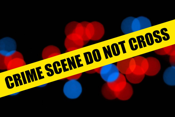 Close-up gele barricade tape met plaats delict niet kruisen woorden over politie achtergrond van wazig rood en blauw politie lichten bokeh - Foto, afbeelding