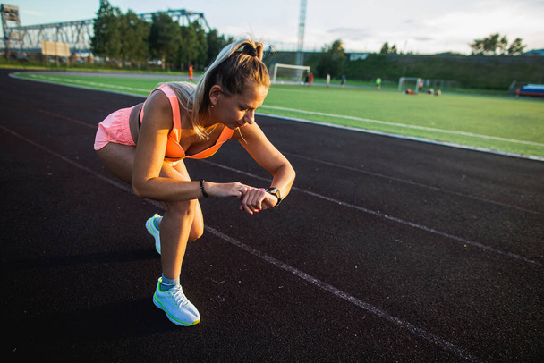 Sports girl starts training on smart watch before the race at the stadium - Foto, Bild