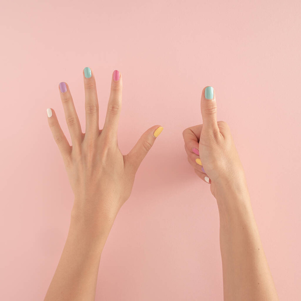naisten kädet värikkäillä kynsillä pastellin vaaleanpunaisella taustalla. Kopioi kesällä moderni trooppinen abstrakti taide naisten kädellä. minimaalinen tausta idea numero kuusi - Valokuva, kuva
