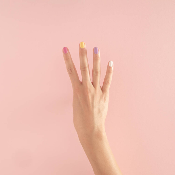 ženy ruce s barevnými nehty na pastelově růžovém pozadí. kopírovat prostor. léto moderní tropické abstraktní umění s ženskou rukou. minimální pozadí nápad s číslem čtyři - Fotografie, Obrázek