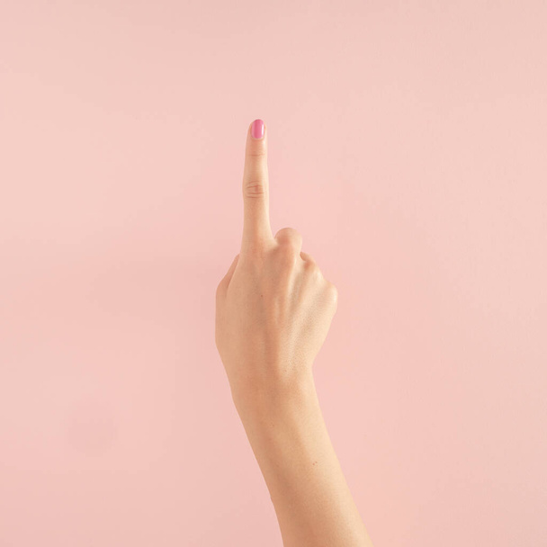 ręce kobiet z kolorowymi paznokciami na pastelowym różowym tle. skopiować przestrzeń. latem nowoczesna tropikalna abstrakcyjna sztuka z kobiecą ręką. minimalny pomysł na tło z numerem jeden - Zdjęcie, obraz