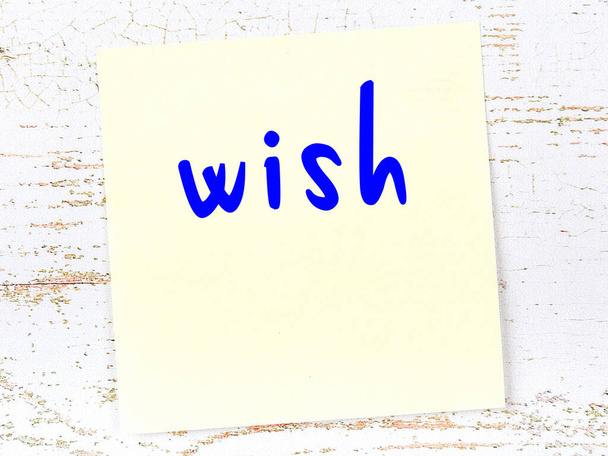 Concept of reminder about wish. Yellow sticky sheet of paper on wooden wall with inscription - Fotoğraf, Görsel