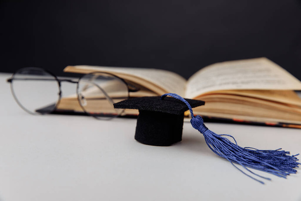 Maturitní čepice a brýle s otevřenou knihou na stole. Zaměření na klobouk - Fotografie, Obrázek
