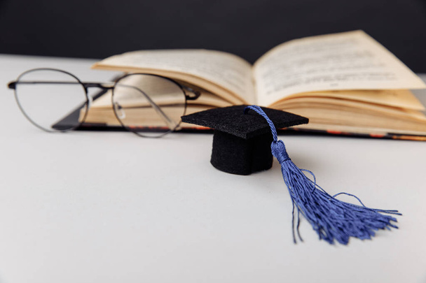 Mütze und Brille mit Buch auf weißem Tisch. Bildungs- und Wissenschaftskonzept - Foto, Bild