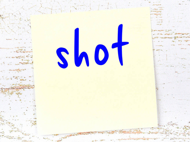 Концепция напоминания о выстреле. Желтый липкий лист бумаги на деревянной стене с надписью - Фото, изображение