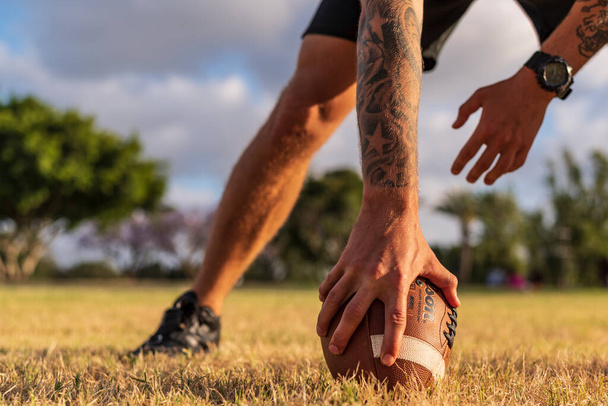 23.05.2020. American football ball in players hand on green lawn - 写真・画像