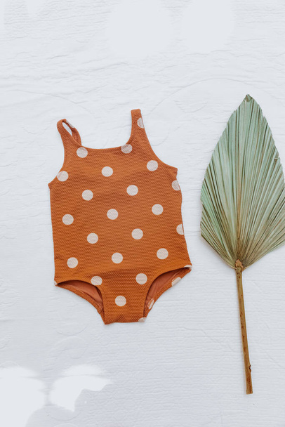 Still life baby summer concept. Vintage baby swimsuit with palm leaf  on white background. Summer concept for kids,  Top view, flat lay, copy space  - Foto, Bild