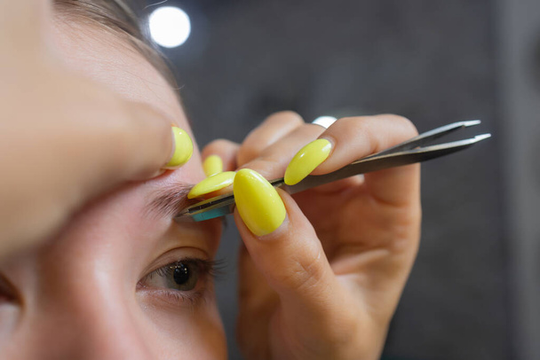 Beautician making depilation with wax strip young womans eyebrows in spa center. Attractive woman getting facial care at beauty salon. - Foto, Imagem