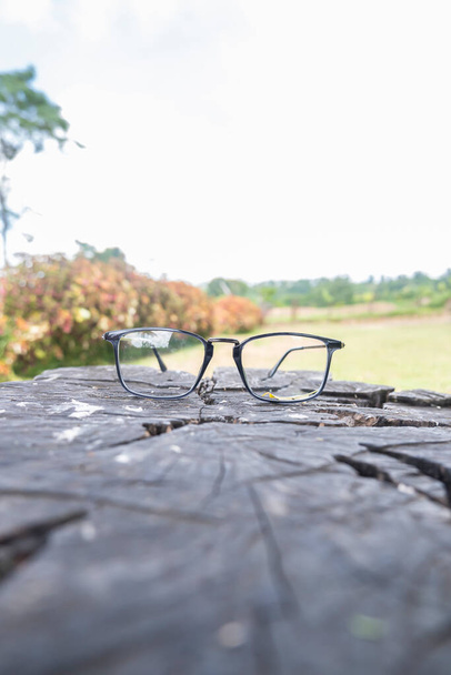 czarna kwadratowa rama okularów na starym drewnie. kwadratowa ramka na zdjęciu z przodu z naturalnym tłem krajobrazu - Zdjęcie, obraz