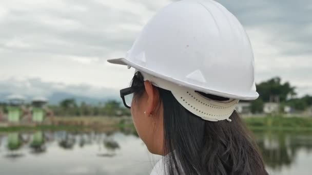 Female engineer takes off her safety helmet while relaxing beside the dam construction site to generate electricity. - Materiał filmowy, wideo