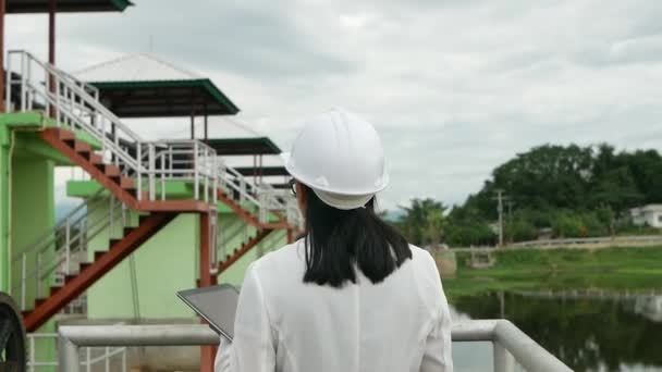 Beyaz kasklı kadın mühendis dijital tabletle çalışıyor ve baraj inşaatındaki radyo iletişimini elektrik üretmek için kullanıyor. Temiz Enerji ve Teknoloji kavramları. - Video, Çekim