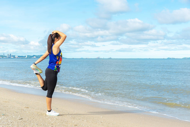 Nuori nainen yllään urheiluvaatteet tekee venyy rannalla, valtameren taustalla. Terve Concep - Valokuva, kuva