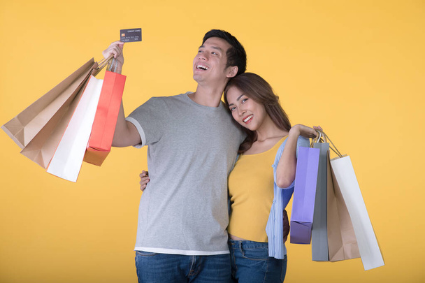 Asian couple holding credit card and shopping bags isolated on yellow background - Фото, зображення