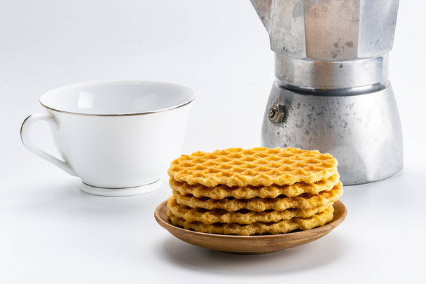 Stack of crispy waffles on a wooden dish with a white ceramic cup of coffee and a moka pot coffee maker on white background with clipping path. - Fotó, kép