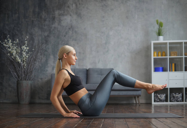 Young and sporty girl in sportswear is doing exercises in home interior. Fit and slender blond woman goes in for sports and fitness. Healthcare, fat burn and wellness. - Fotoğraf, Görsel