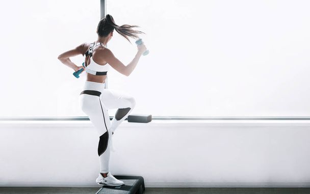 black woman in a white tracksuit in the gym with dumbbells in her hands - Foto, imagen