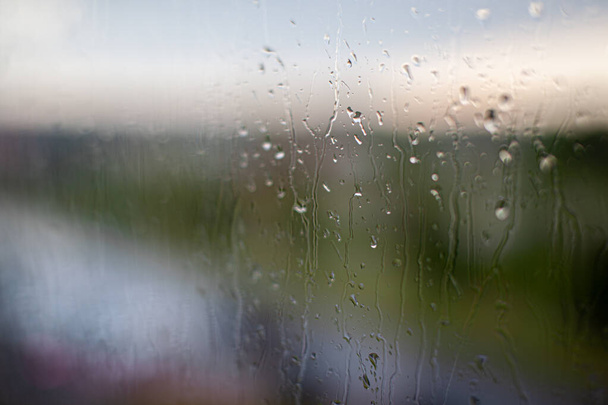 Día lluvioso a través de la ventana en el cielo gris nublado y los edificios de la ciudad de fondo. Concepto. Paisaje urbano nocturno detrás de la ventana de cristal con gotas de agua goteantes. - Foto, Imagen