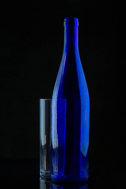 Натюрморт с голубой бутылкой и стеклом на черном фоне - Фото, изображение
