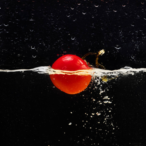 Fresh red tomato falling into water with water splash and air bubbles isolated on black background. - Foto, afbeelding
