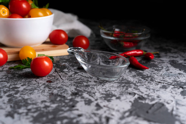 empty sauce cup or dish on a dark surface flat lay, different vegetables around, pepper, tomatoes b - Foto, imagen