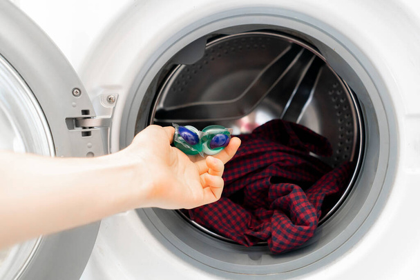 Personen legen spezielle Putzkapseln oder -kapseln mit schmutzigem Tuch in die Waschmaschine - Foto, Bild
