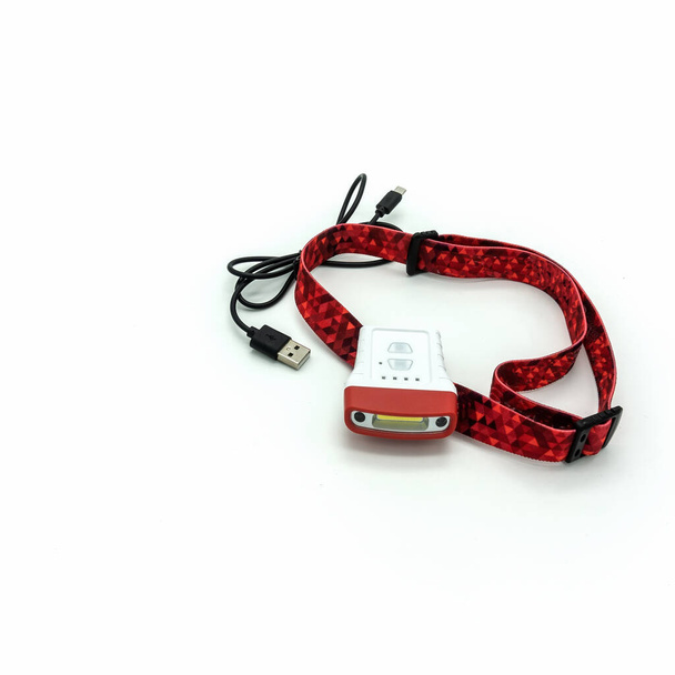 Flashlight for a cyclist. Wi-Fi connection and light control buttons on the case. Red elastic headband. Wire with usb connector for charging. Isolated on a white background. - Photo, Image