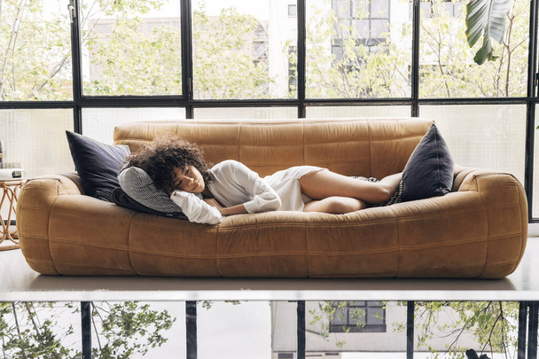Pensive young african american woman lying on a yellow sofa in a beautiful loft. Home concept. - Fotoğraf, Görsel