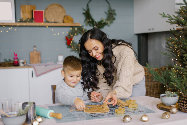 Küçük oğlu olan mutlu bir anne mutfaktaki hamurdan Noel kurabiyesi kalıplarını kesiyor ve gülüyor.. - Fotoğraf, Görsel