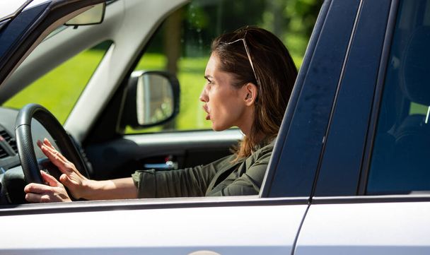 Egy fiatal nő úthengerrel szürke autót vezet. Frusztrált lány nyomja autó kürt agresszív a forgalom. - Fotó, kép