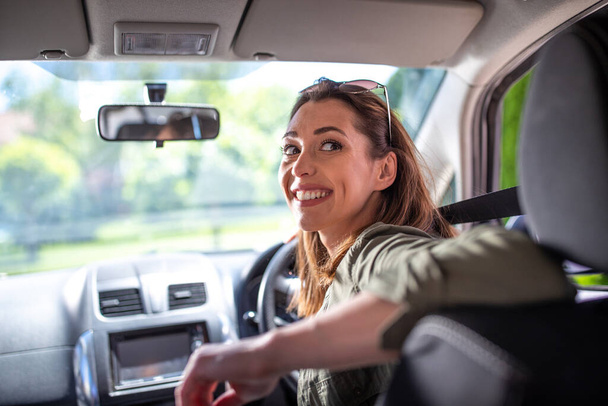 Hübsche junge Autofahrerin lächelt. Attraktive Frau im Rückwärtsgang schaut über die Schulter.  - Foto, Bild