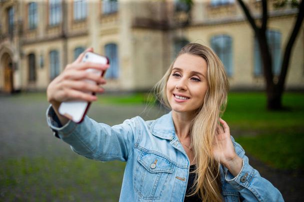 Kot ceketli güzel, modern moda bir kız telefonda selfie çekiyor. - Fotoğraf, Görsel