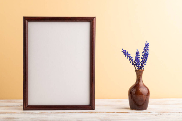 Wooden frame with blue muscari hyacinth flowers in ceramic vase on orange pastel background. side view, copy space, still life, mockup, template, spring, summer minimalism concept. - Photo, Image