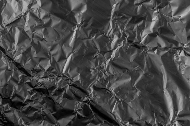 Černá rozdrcená poškozená hliníková kovová fólie. Grunge vrásky. Abstraktní tmavé pozadí - Fotografie, Obrázek