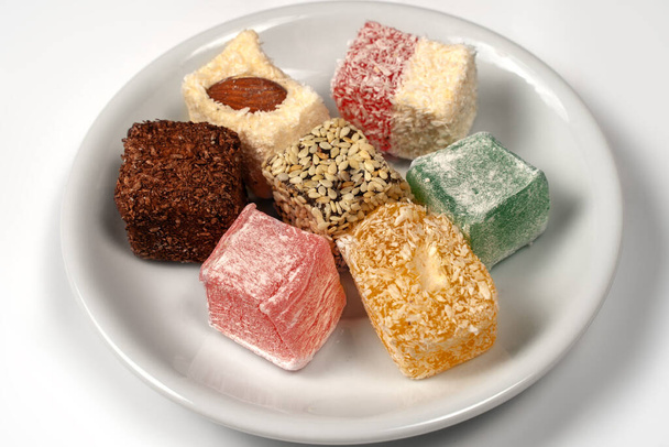 Many pieces of Turkish Delight set on a pile on little white plate. Empty background. Colorful sweet cubes of lokum. Eastern traditional dessert. Copy space. - Fotografie, Obrázek