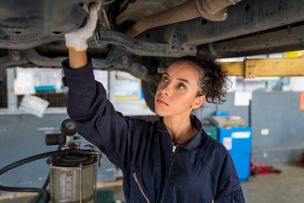 Servicio de reparación concepto de mantenimiento. Mujer afroamericana trabaja para mecánico de automóviles en el garaje comprobando el motor del coche. Un mecánico de automóviles está cambiando el aceite en un taller de reparación de automóviles. - Foto, Imagen