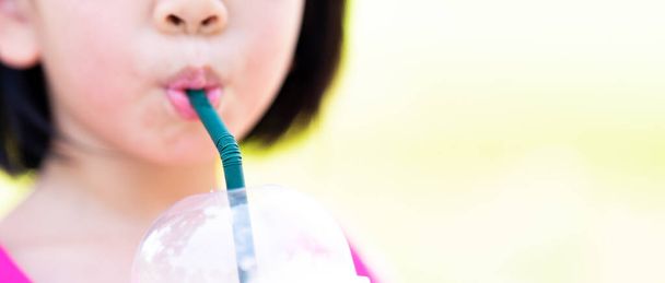 Kesilmiş görüntüler. Asyalı çocuk yeşil pipetle plastik bardaktan su emiyor. Sinematik oran. - Fotoğraf, Görsel