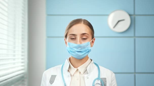 Blonde lady doctor takes blue disposable face mask off - Footage, Video