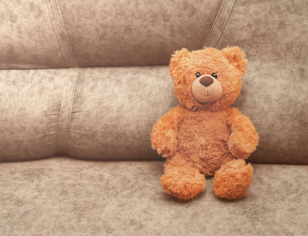 Το αρκουδάκι κάθεται σε έναν καναπέ και κοιτάζει έναν θεατή. έννοια της ασφάλειας και της μοναξιάς των παιδιών, τα παιδιά καλύτερος φίλος - Φωτογραφία, εικόνα