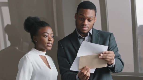 Happy young African businessman and businesswoman holding papers check sales statistics looking at financial report celebrate business success, feels motivated by great achievements good work result - Footage, Video
