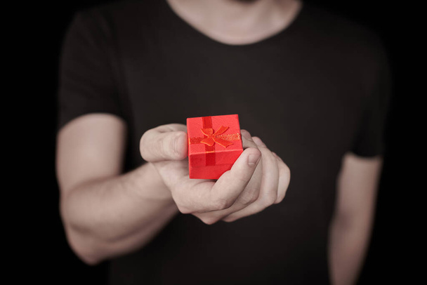 Red gift box in hand. Valentine gift. Small anniversary giftbox from man. Little surprise concept. Black background. - Photo, Image