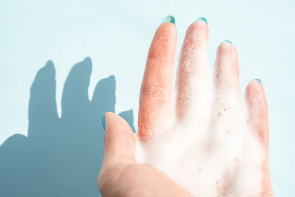 vrouwelijke hand in wit schuim op een blauwe achtergrond. - Foto, afbeelding