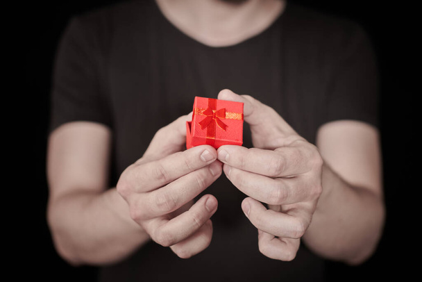 Man give a gift in red gift box. Opening Valentine gift. Small anniversary giftbox from man. Little surprise concept. Black background. - Photo, Image