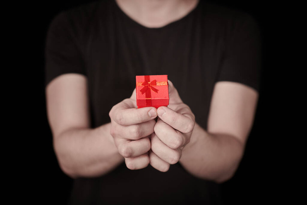 Κόκκινο κουτί δώρου στο χέρι. Δώρο Αγίου Βαλεντίνου. Ένα μικρό δώρο επετείου από τον άνθρωπο. Μια μικρή ιδέα έκπληξη. Μαύρο φόντο. - Φωτογραφία, εικόνα