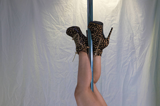 Detail of pole dancer's feet with leopard heels. The feet are entangled in the pole while the pole is held upside down. Dance concept - Photo, Image