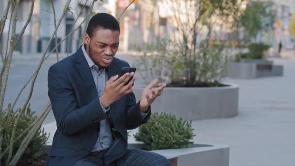 Gekke gestresste zwarte man houdt mobiele telefoon geïrriteerd met een foutmelding spam, langzaam vast gebroken smartphone, boos gefrustreerde Afrikaanse zakenman door mobiele telefoon probleem met klachten over slechte service - Video