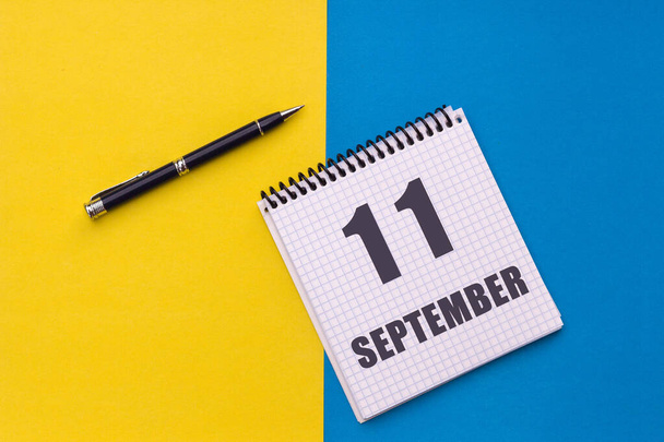 11 вересня. 11 день місяця, дата календаря. Блокнот з спіраллю і ручкою лежить на жовто-блакитному фоні
. - Фото, зображення