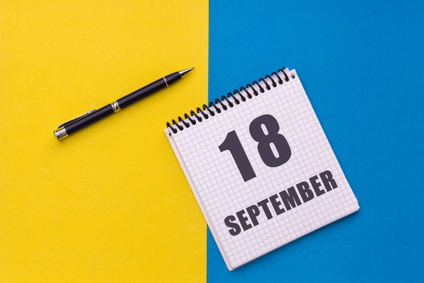 18 de Setembro. Dia 18 do mês, data do calendário. Notebook com uma espiral e caneta encontra-se em um fundo amarelo-azul. - Foto, Imagem