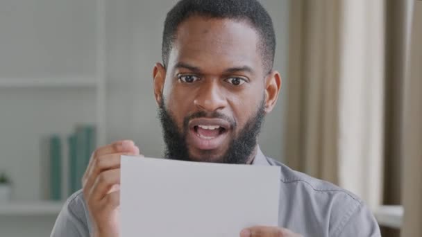 Возбужденный чернокожий мужчина-руководитель получает почту с выплатой заработной платы, одобрением бизнес-кредита. Счастливый бизнесмен открывает конверт, читая хорошие новости в бумажном письме, сидя на рабочем месте - Кадры, видео